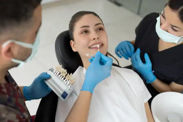 Dentist matching veneer shade to female patient's teeth during cosmetic consultation